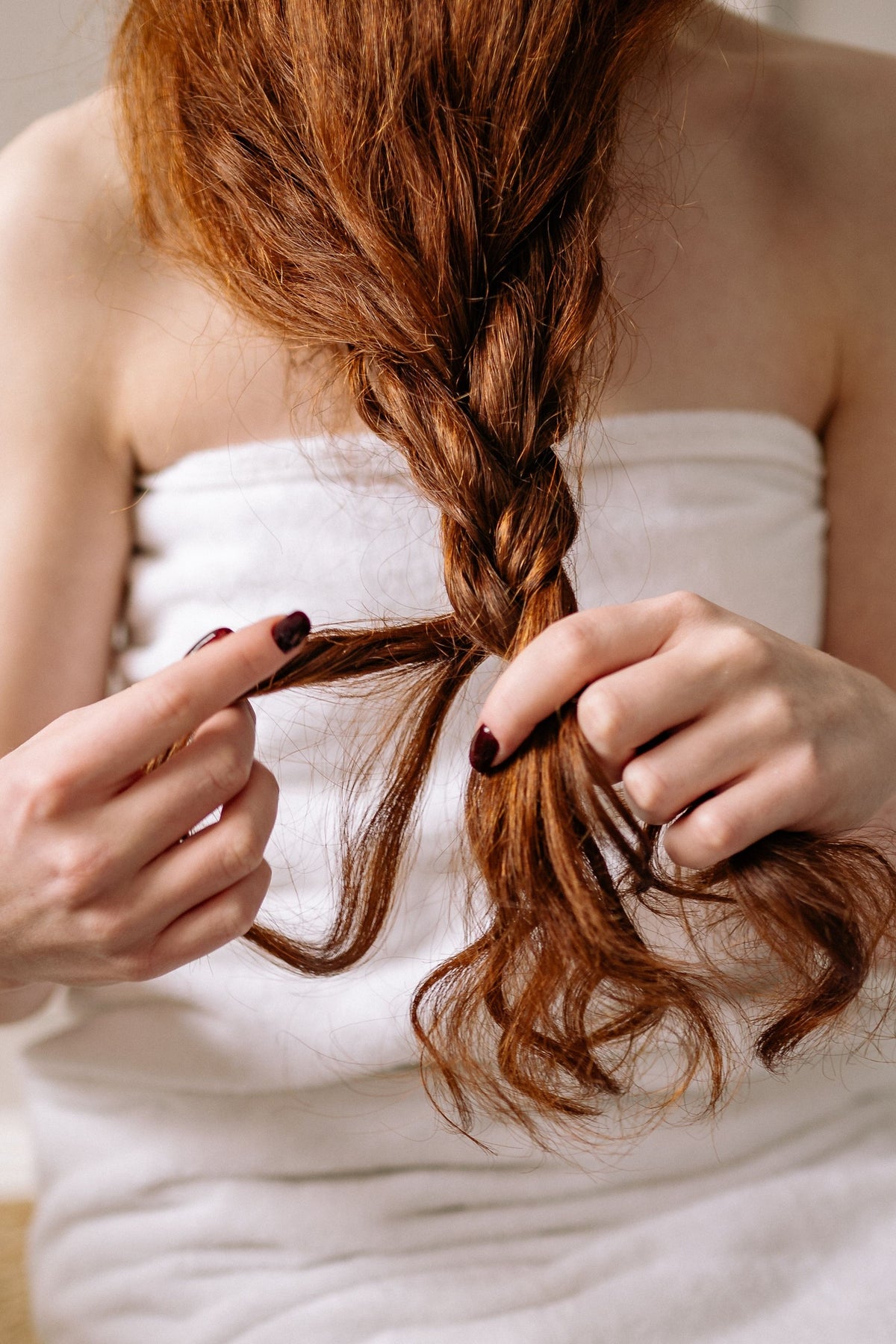 Woman wrapped in a bath towel braiding dry hair caused by hard water minerals, chlorine, and imbalanced water pH.