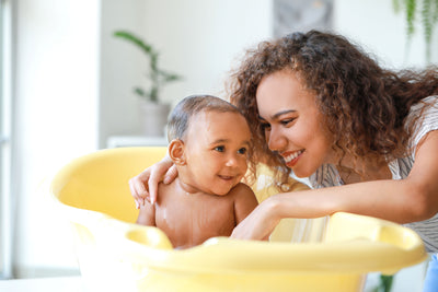 Smiling mother bathing her baby in a yellow tub using household water checked with a Kleer Blue Water test kit.